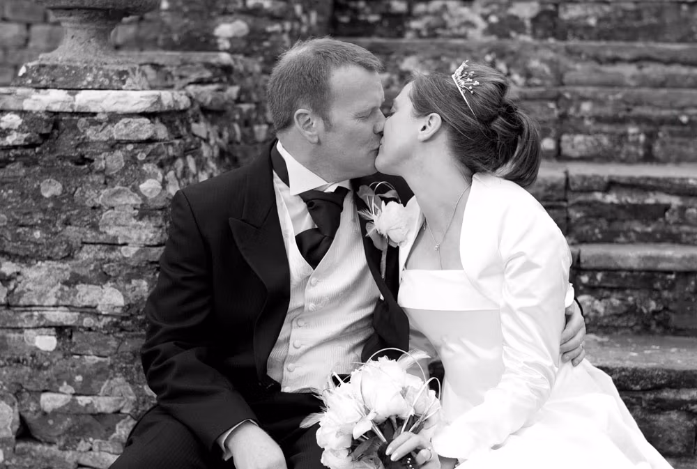 Alison and Hamish sitting together on the steps, sharing a kiss in black and white.