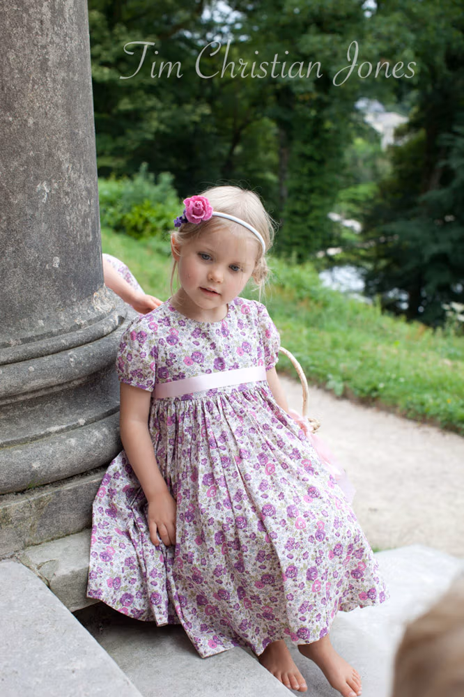Little flower girl resting on the stone steps, surrounded by summer greenery

