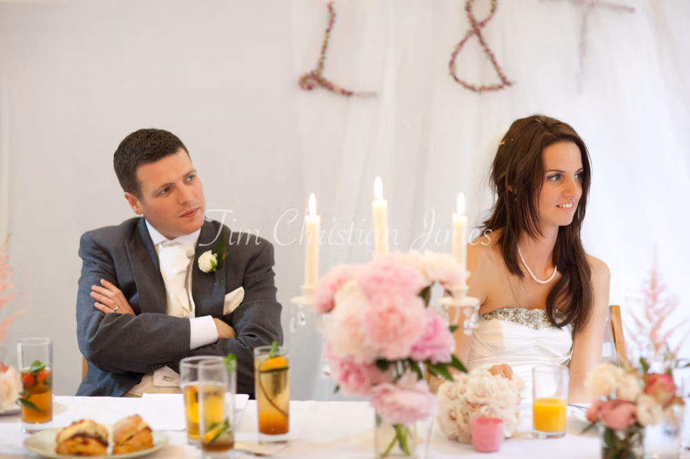 Groom folds his arms and smiles as the bride looks cautiously amused