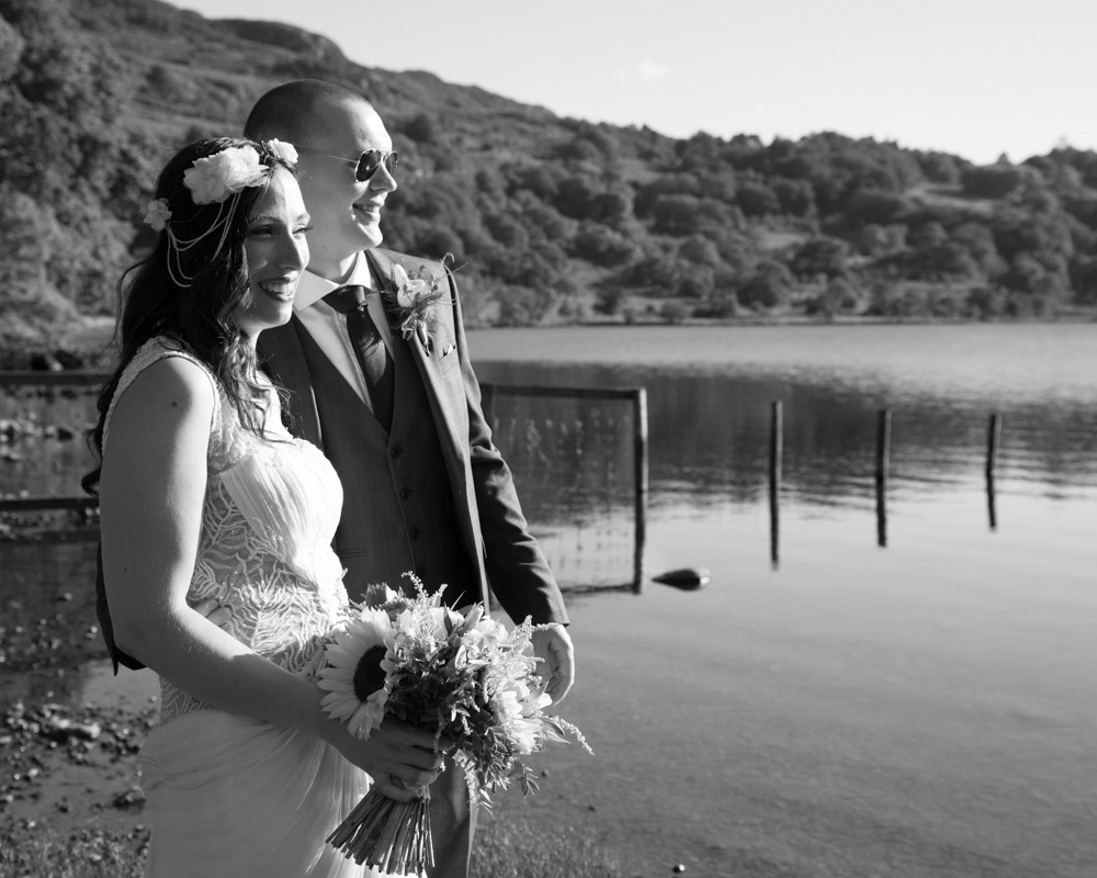 Same couple smiling more widely in black and white by the lake.