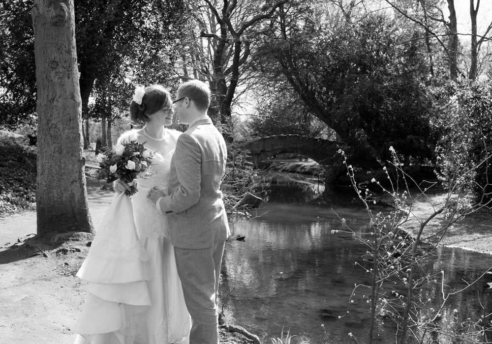 Bride holds her bouquet and dress in black and white by the river at Golden Acre Park.
