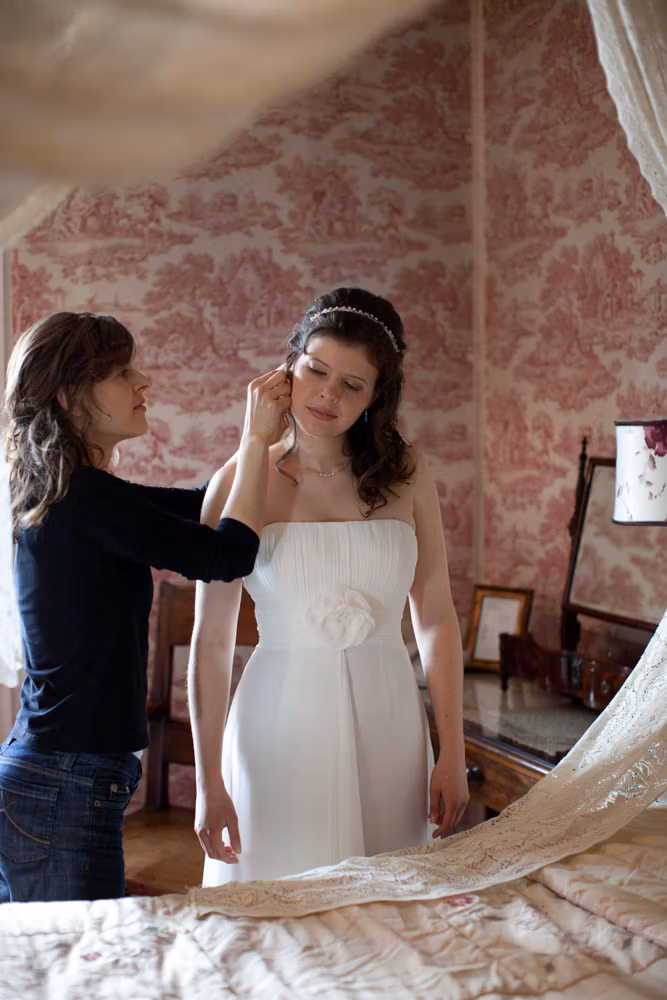 A candid view of the bride and bridesmaid seen through the frame of the four-poster bed