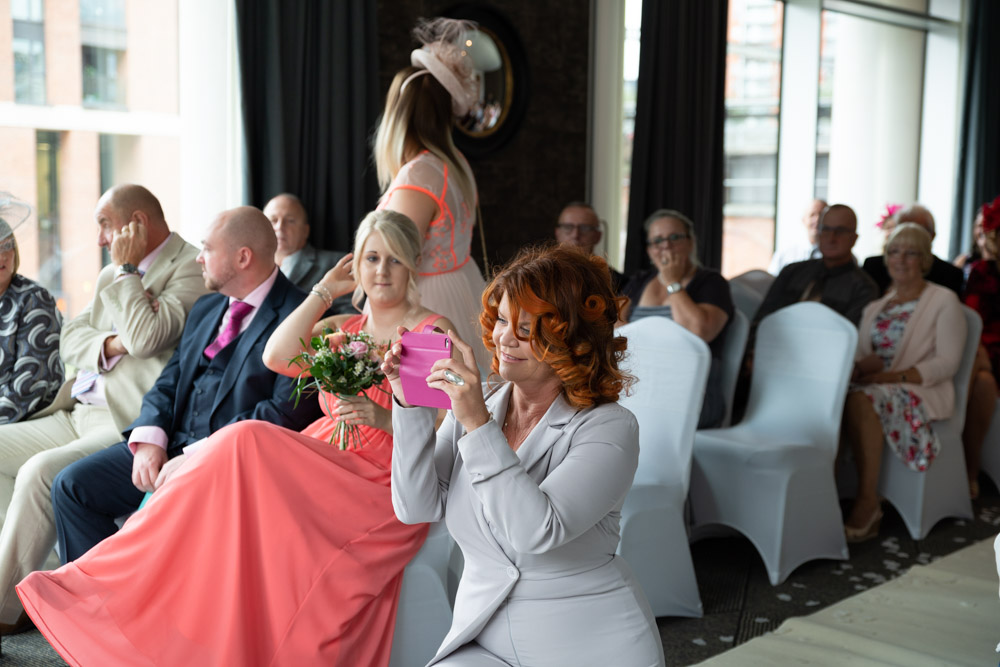 A guest kneels to photograph the couple from a creative angle