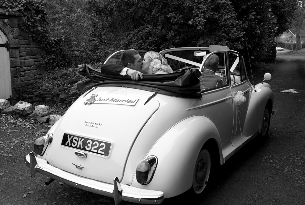 Dani and Scott kiss in a white Morris Minor 1000 with top down