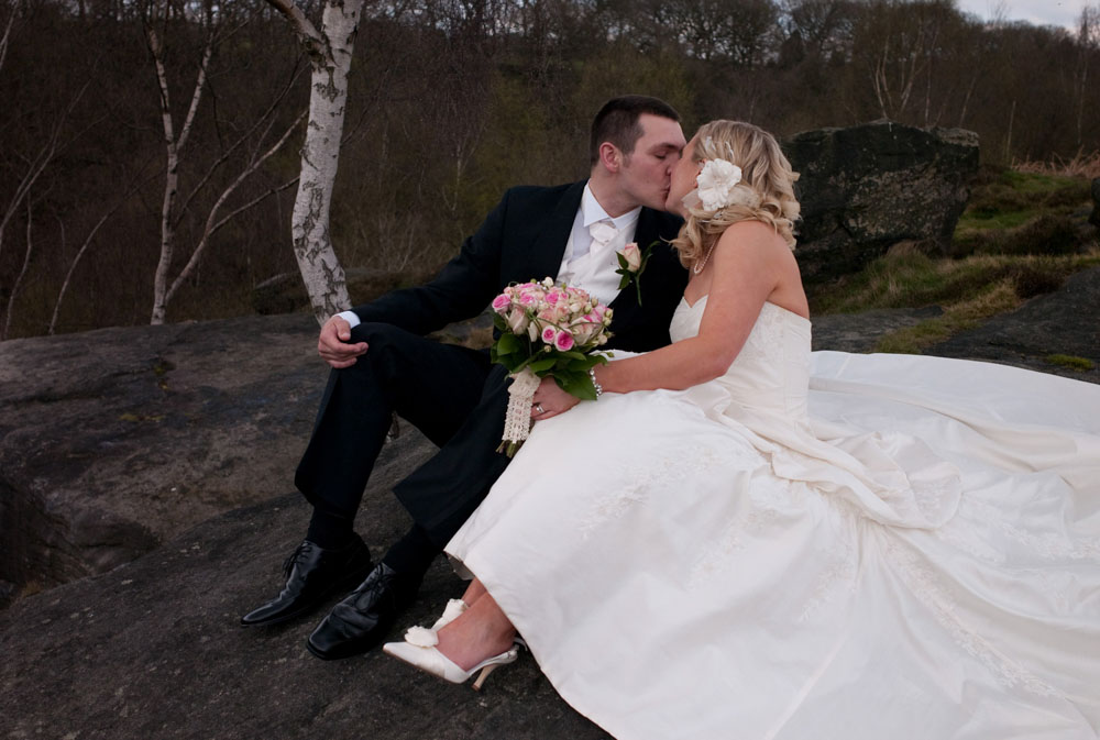 Dani and Scott kiss while sitting on rocks, her dress flowing out