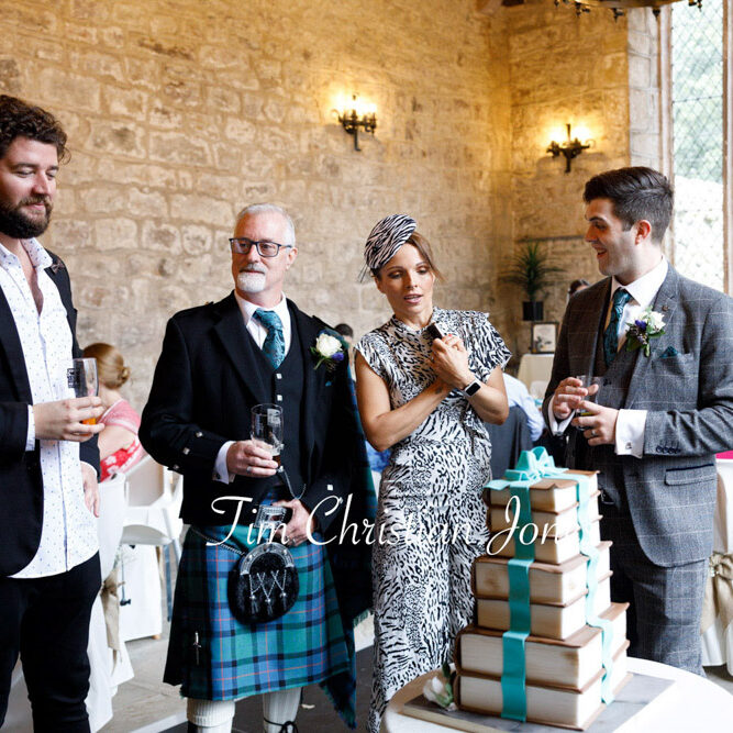 Smiling guests gather around the wedding cake at Barden Tower.