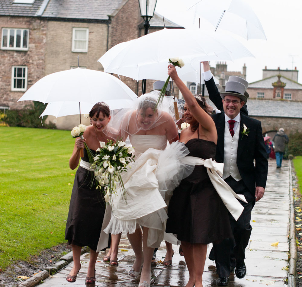 The bride and her bridal party walk up the path to the church, each carrying a white umbrella against the soft Yorkshire rain.