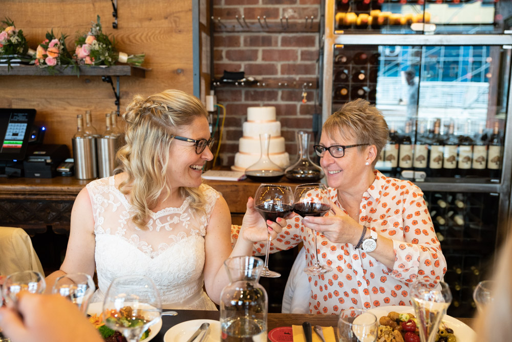 The couple clink wine glasses with the wedding cake behind