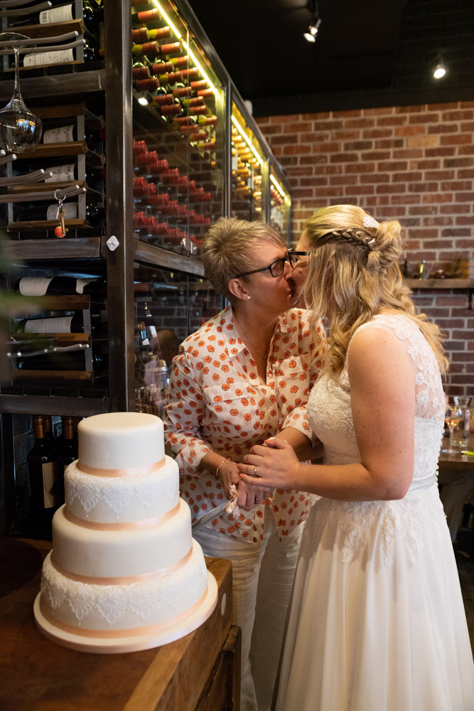 The couple kiss while holding the wedding cake knife
