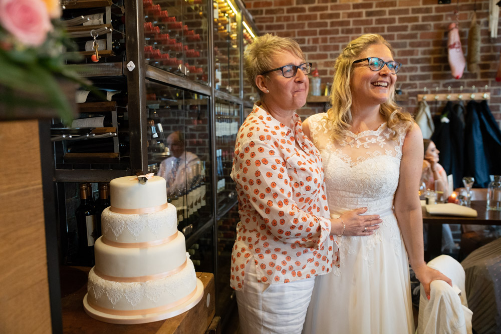 Clare and Tracey pose for guests by the wedding cake