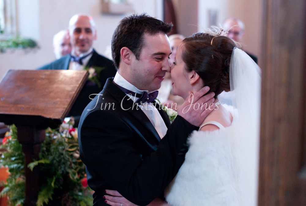 Moments after their first kiss, the couple smile with noses touching, soft light and joy shared quietly between them.
