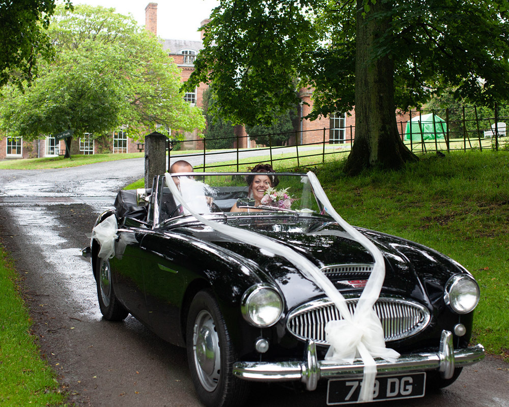 Couple smiling as they drive through venue gates, ready to pause for portraits.