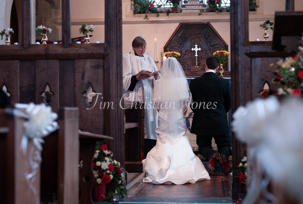 The couple kneel together at the altar as the vicar reads a blessing, a quiet moment of reflection during the ceremony.