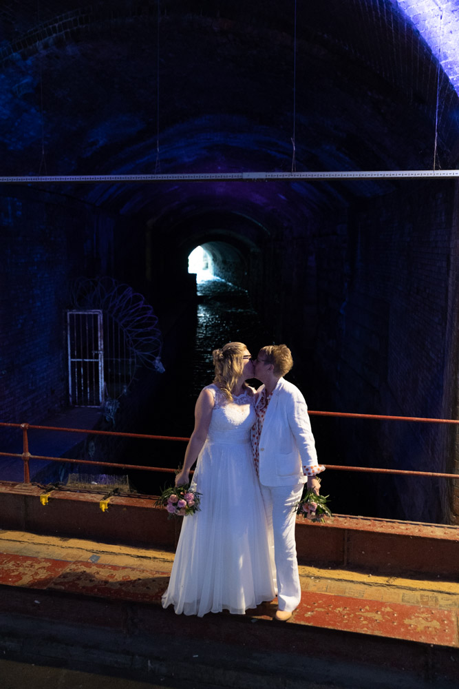 Clare and Tracey kiss beneath the blue-lit Granary Wharf arch