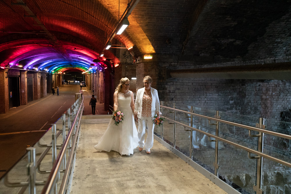 Halfway across the footbridge under colourful tunnel lights, holding hands