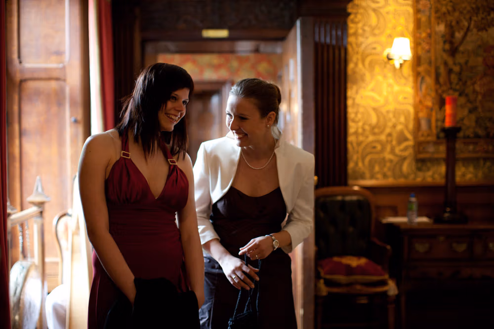 Two well-dressed women sharing a laugh in the ceremony room before it begins