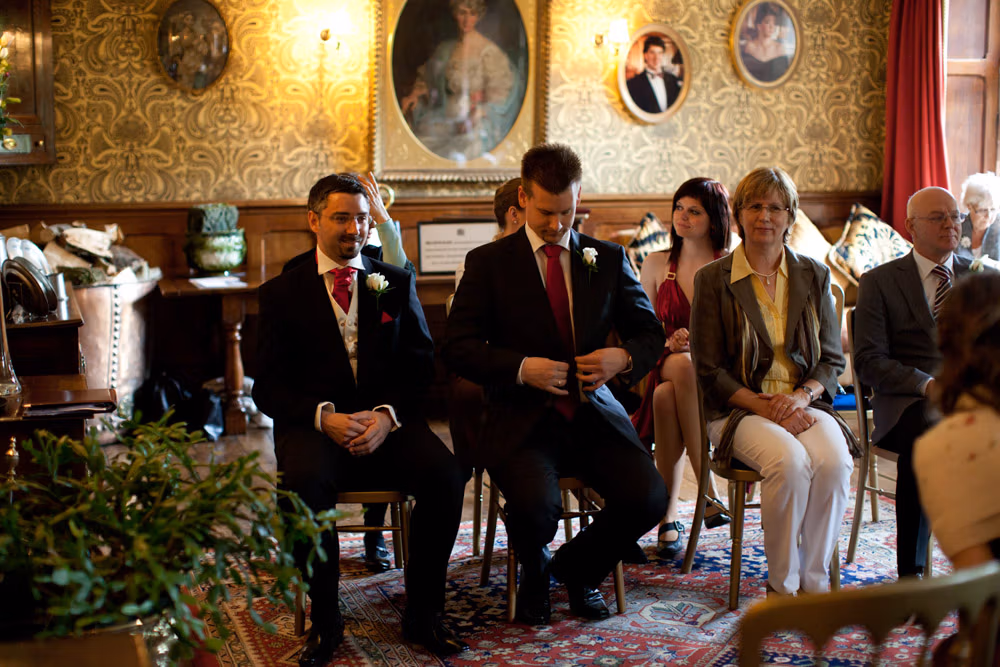 Groom, best man, and guests seated and waiting for the ceremony to begin at Soughton Hall