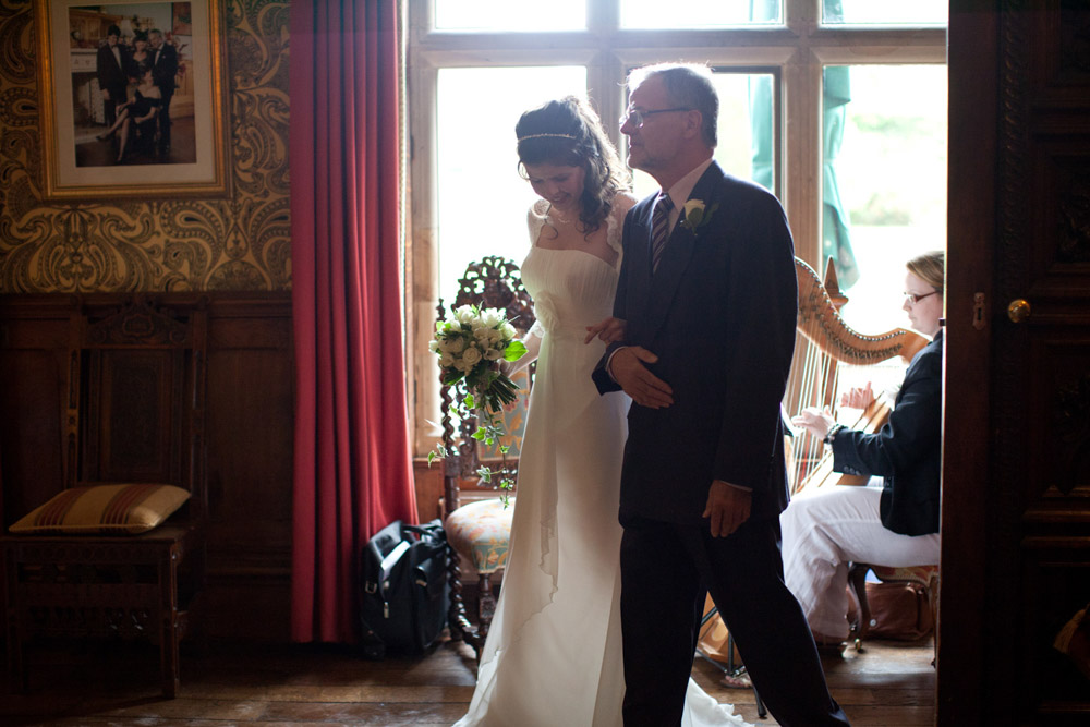 Bride and father walking past a window filled with soft misty light