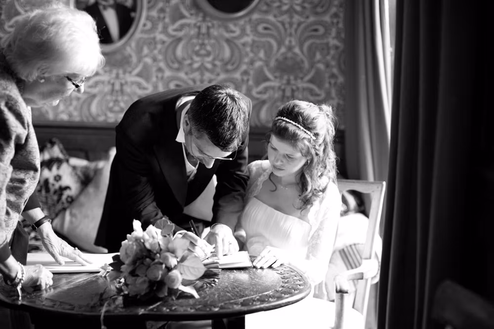 Bride watching groom sign the register in black and white