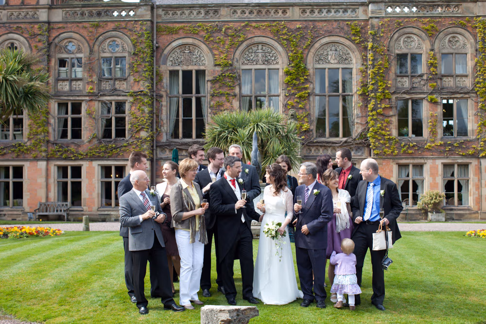 The full wedding party gathered outside Soughton Hall, standing on the lawn in front of the grand façade