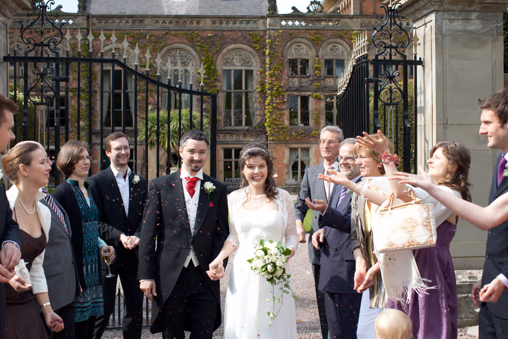 Couple smiling as light confetti floats down outside the gates of Soughton Hall