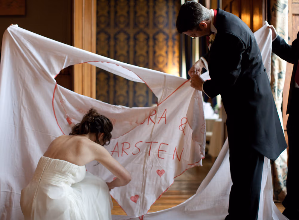 Bride crouched down finishing the cut while groom holds the top of the heart shape