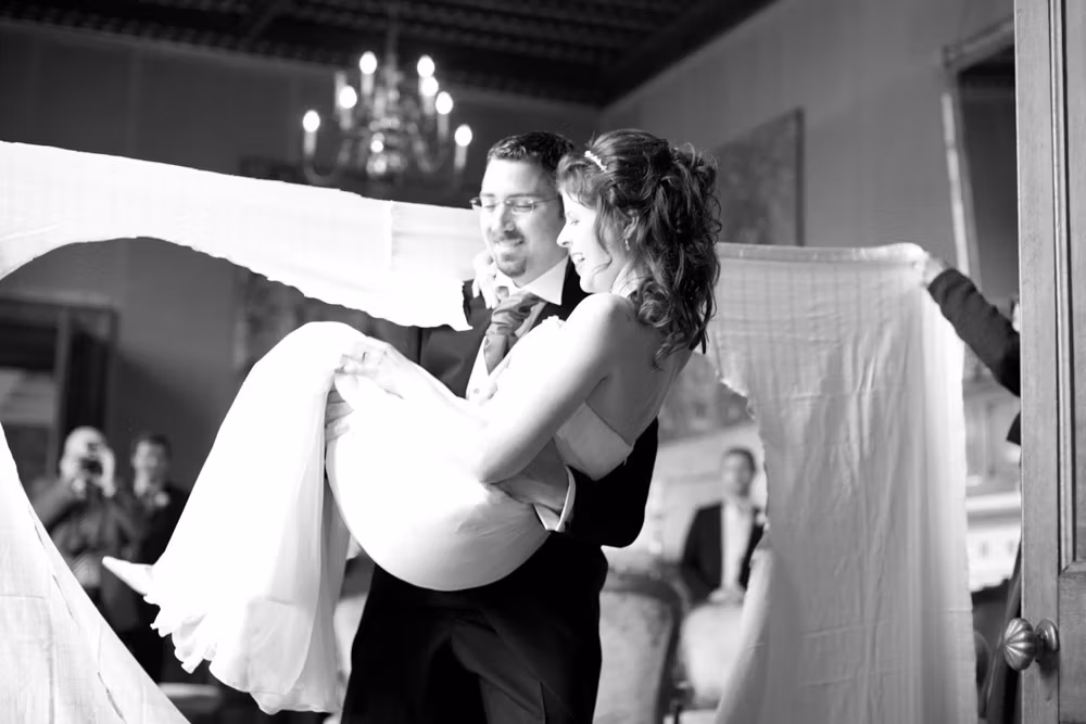 Groom lifts and carries bride through the heart-shaped opening in the sheet