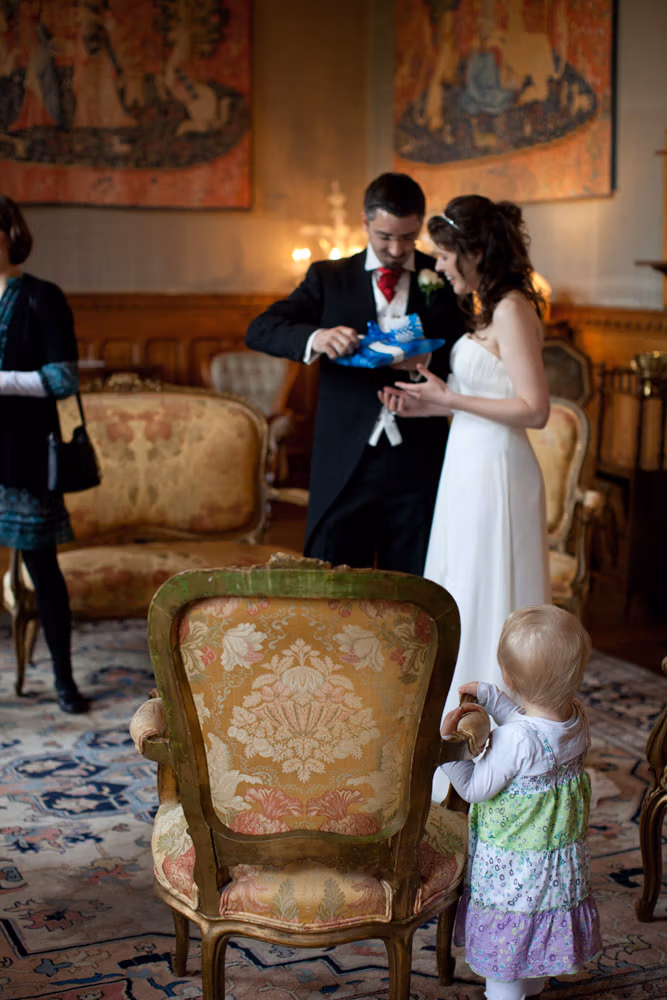 A young child standing by a chair watching the couple admire their gifts