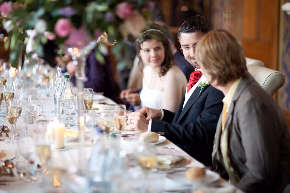 Groom seated, relaxed, chatting with guests at the end of the wedding breakfast