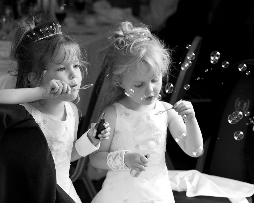 Bridesmaids blow bubbles at the table, stealing the spotlight with childlike wonder.